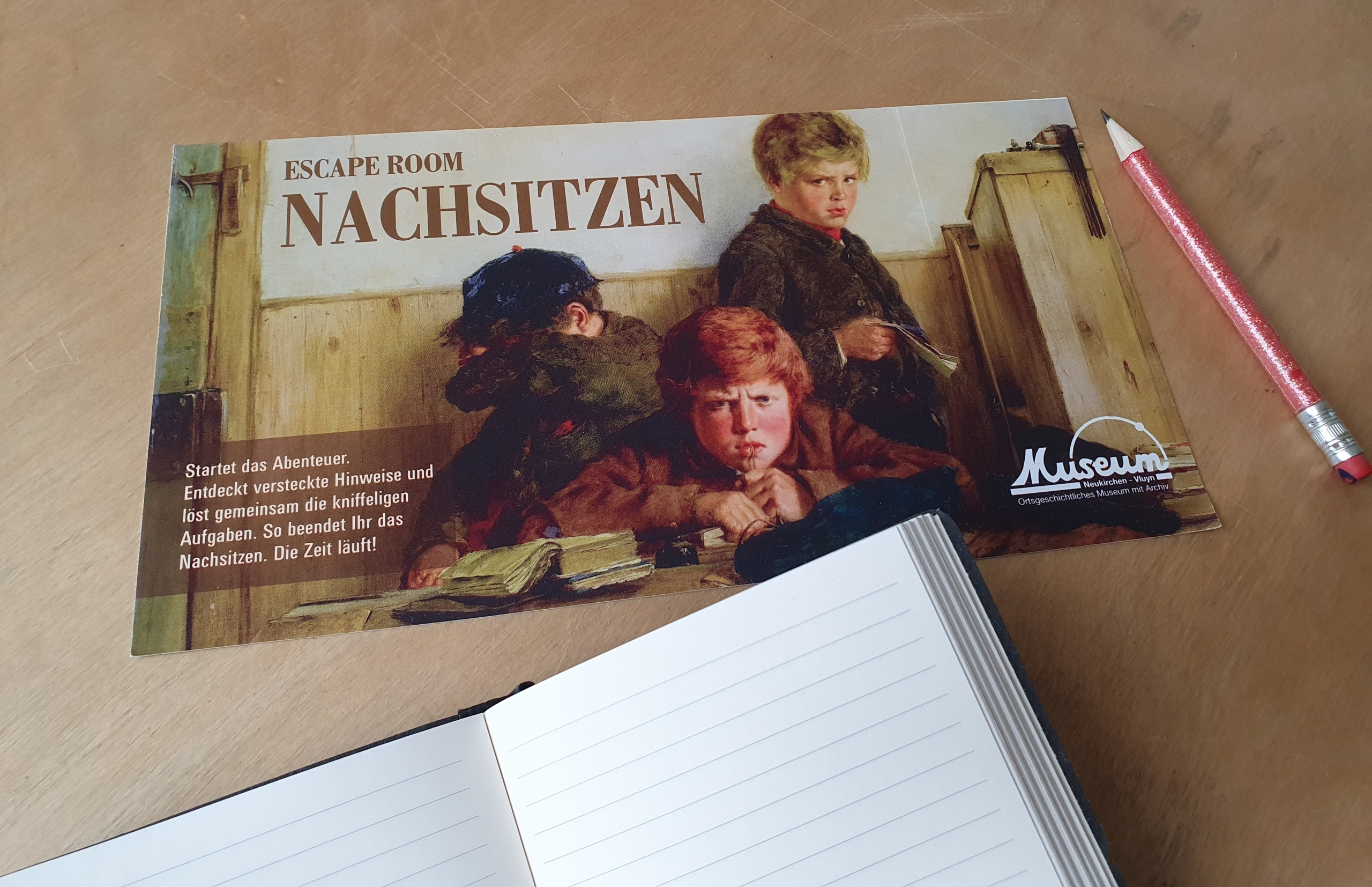 Flyer für den Escape Room "Nachsitzen" im Heimatmuseum Neukirchen-Vluyn mit Notizblock und Stift.